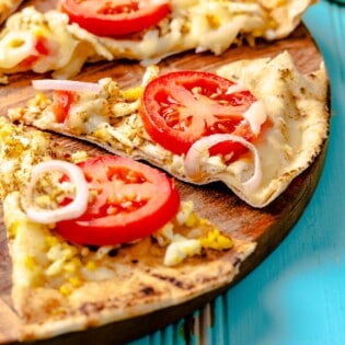 a pita breakfast pizza on a wooden serving platter sliced into individual pieces.