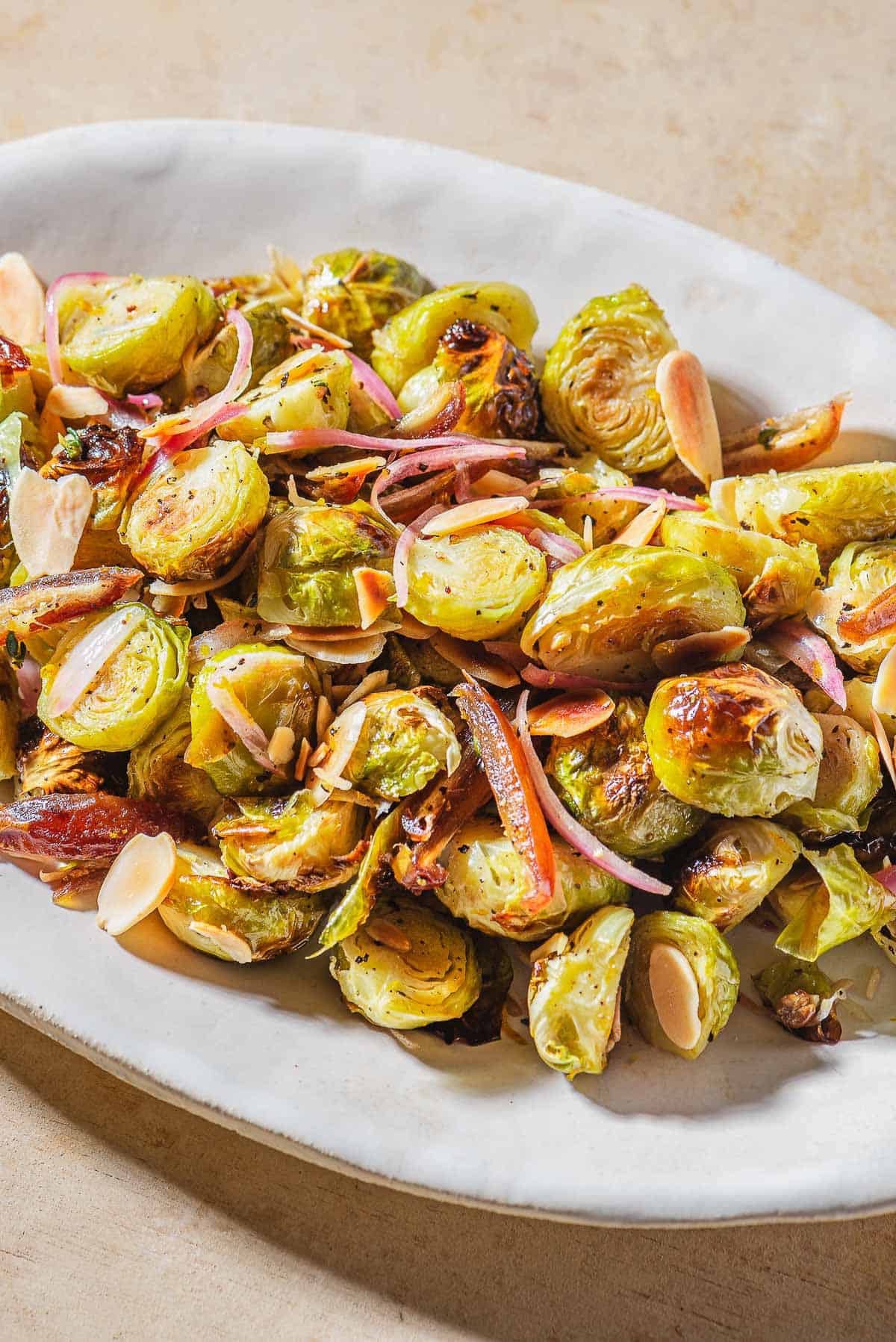 A close up of roasted brussels sprouts with dates and almonds on a platter.