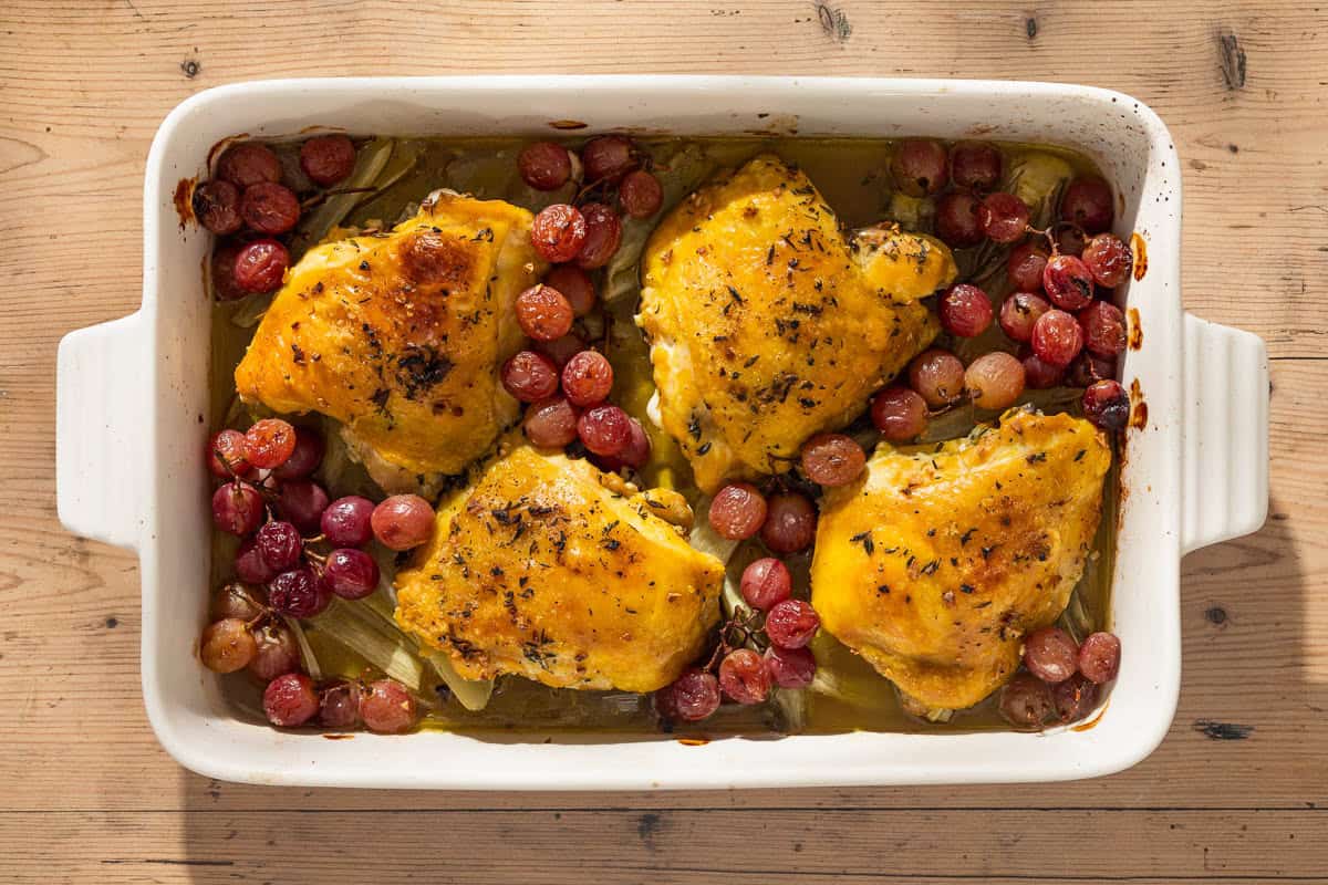 A overhead photo of 4 braised chicken thighs in a baking dish with grapes and fennel.