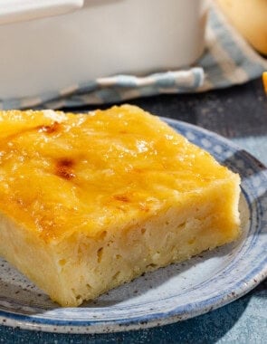 A close up of a piece of portokalopita greek orange cake on a plate next to another plate with orange wedges.