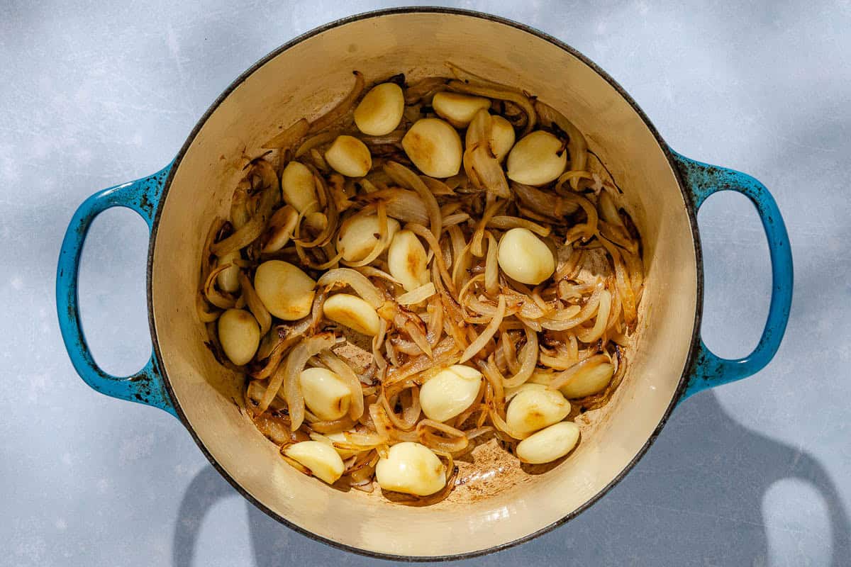 An overhead photo of caramelized garlic cloves and onions in a large pot.