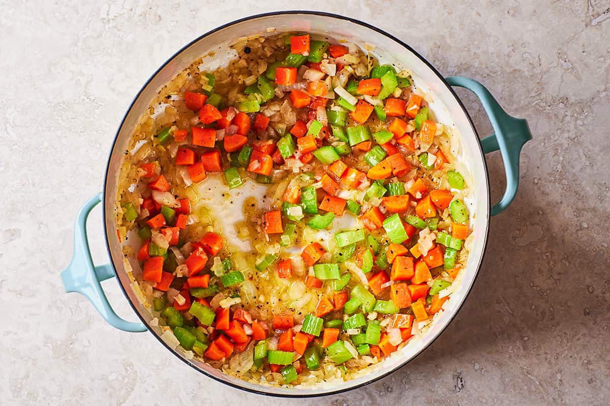 chopped onions, garlic, carrots and celery being sautéed in a large pot.