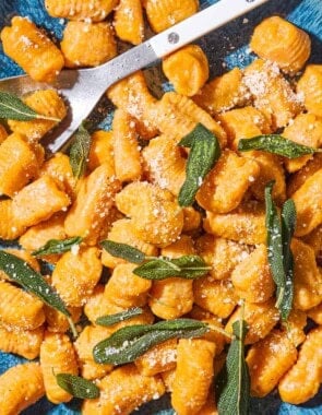 A close up of sweet potato gnocchi and sauce topped with fresh sage on a serving platter with a serving spoon spoon.